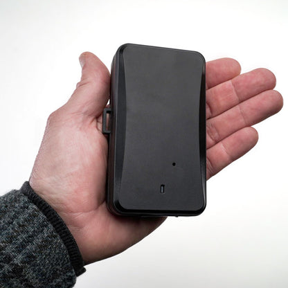 The black Logistimatics Protect Plus GPS Tracker is shown in someone's palm, highlighting its compact dimensions that allow for discreet placement and monitoring of valuable assets.